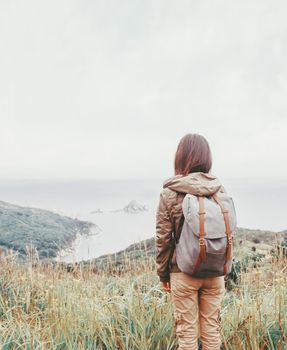 Traveler backpacker young woman walking in the mountains on coastline in summer, rear view.