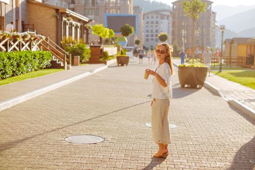 Stylish young woman wearing in white clothing walking on the street with paper cup of coffee in the morning, city lifestyle.