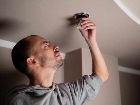 The man unscrews a broken old lamp. Installation of ceiling lighting.