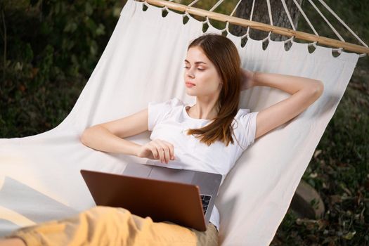 woman outdoors with laptop lies in hammock leisure technology. High quality photo