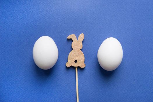 Easter background, white eggs and a wooden hare on a blue background, flatlay, top view, empty space for text.