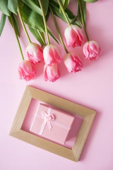 Pink Tulip flowers, photo frame and gift box are arranged on a pink background. The view from the top, smooth lay. The concept of spring. Women's day. Mother's day.