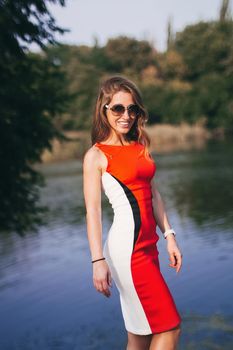 Beautiful smiling young woman girl looking at you in bright red dress outside.