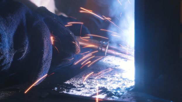 A welder in helmet doing his job. Welding process. Smoke and sparks. Close up shot