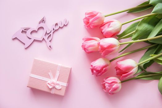 Pink Tulip flowers, a tree cutting and a gift box are placed on a pink background. The view from the top, smooth lay. The concept of spring. Women's day. Valentine's day. Wooden inscription I love you.