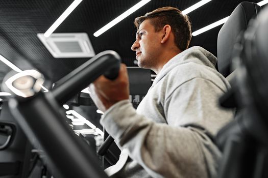 Young fit bodybuilder man doing arms workout training in the gym on machine, close up