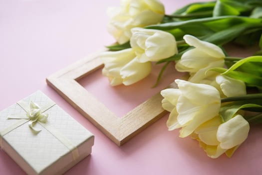 Yellow Tulip flowers, photo frame and gift box are arranged on a pink background. The view from the top, smooth lay. The concept of spring. Women's day. Mother's day.