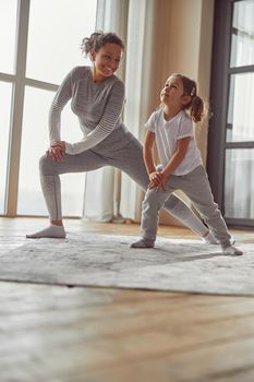 Low angle of smiling mother looking at little girl with love while exercising together indoors