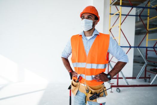 Portrait of mixed race man builder in workwear and hardhat wearing medical mask, close up photo