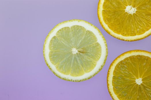 three orange and lemon slices on lilac background