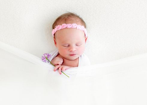 Sleeping newborn baby girl with flowers wrapped in white blanket