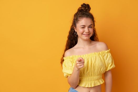 Curly young smiling woman pointing on you against yellow background, close up