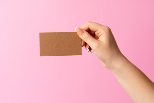 Woman hand showing blank business card on pink background. Close up.