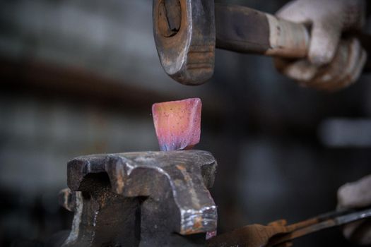 Workspace of blacksmith. Blacksmith working with red hot metal workpiece of new hammer in the vise at the forge. Telephoto shot