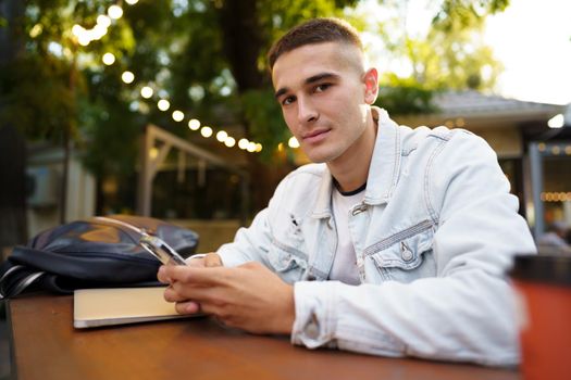 Young man using smartphone while sitting at outdoor cafe, close up