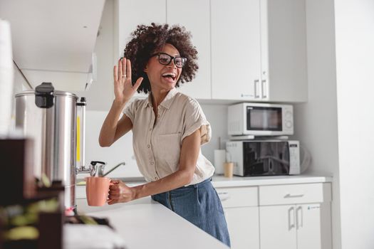 Happy Afro American lady waving to colleague and preparing hot drink on office kitchen