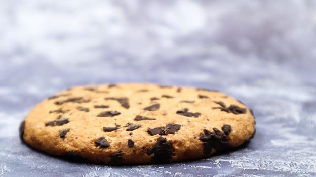 One soft, freshly baked chocolate chip cookie on a gray marble kitchen countertop. American traditional dessert. Delicious sweet food. Homemade baking concept for the holiday. Culinary background.