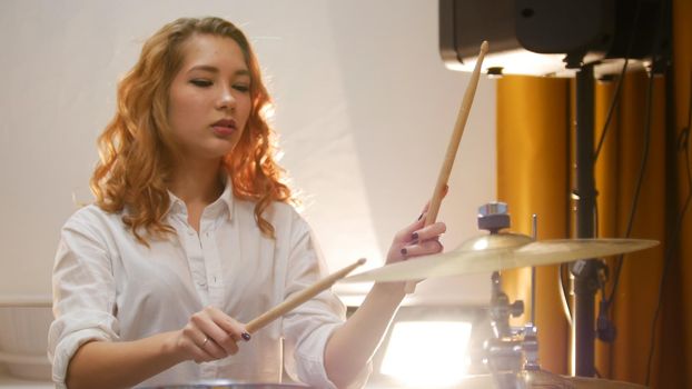 Pretty redhead girl playing drums in studio. Portrait