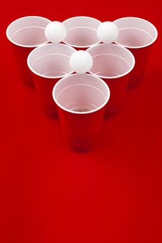 Cups and plastic ball on red background. Beer pong game. Close up.