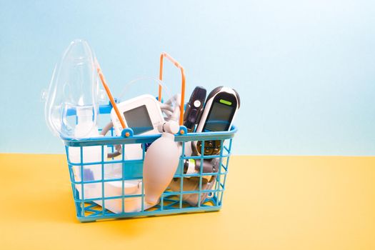 medical devices for home use in a small blue shopping basket, yellow-blue background copy space, glucose meter, inhalation nebulizer, measure blood pressure monitor, online shopping concept