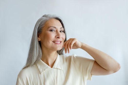 Elegant middle aged woman with hoary hair in shirt poses on light background in studio. Mature beauty lifestyle