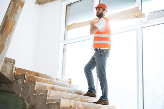 Builder man in hardhat carrying timber on building site, close up portrait