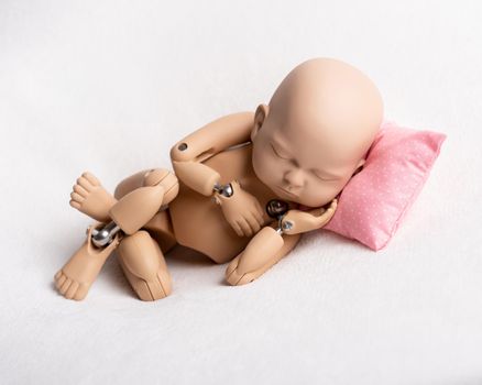 Accurate doll of newborn baby on pink pillow for photo practicing, on white background