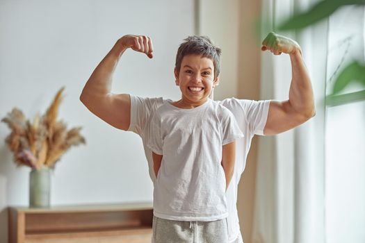 Waist up portrait of smiling son standing before dad who is demonstrating his biceps muscles