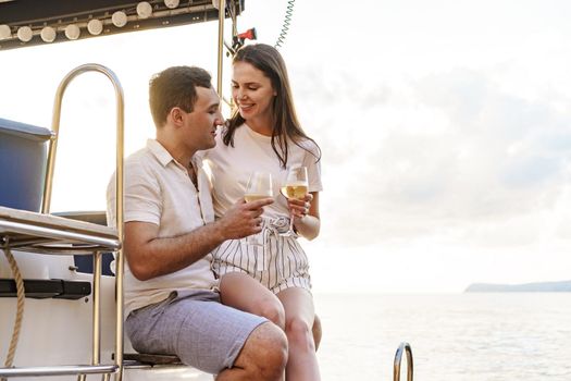 Young loving couple sitting on the yacht deck and drinking wine together