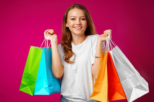 Portrait of happy young smiling woman with shopping bags against pink background