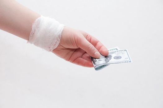 bandaged female hand holds dollar bills on a white background