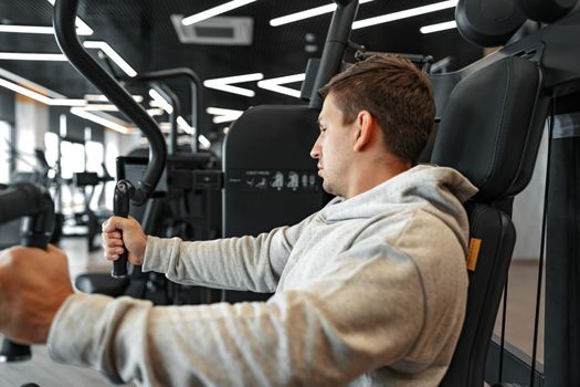 Young fit bodybuilder man doing arms workout training in the gym on machine, close up