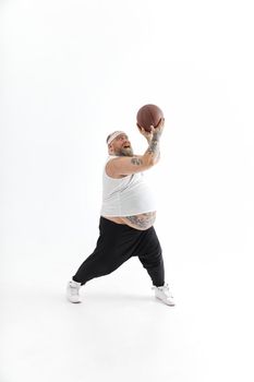 bearded fat caucasian tattoed man with basketball ball in white background. He is funny and happy