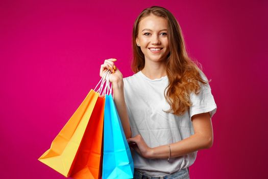 Portrait of happy young smiling woman with shopping bags against pink background