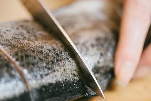 Woman chef cutting raw fish trout for dinner dish in the kitchen, close-up.