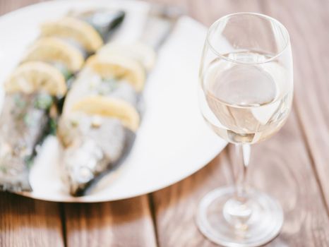 Fish trout dish with lemons on a plate and glass of white wine on wooden table for dinner.