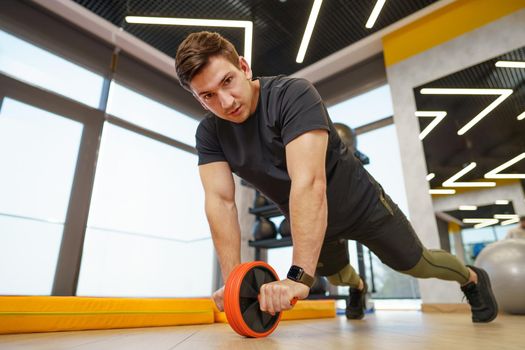 Athlete sporty man doing exercise with abs roller wheel in a gym