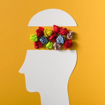 colorful crumpled paper ball inside the paper cut out head on yellow background
