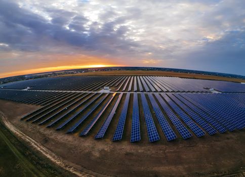 Aerial panorama view of large solar panels at a solar farm at bright summer sunset. Solar cell power plants, colorful photo