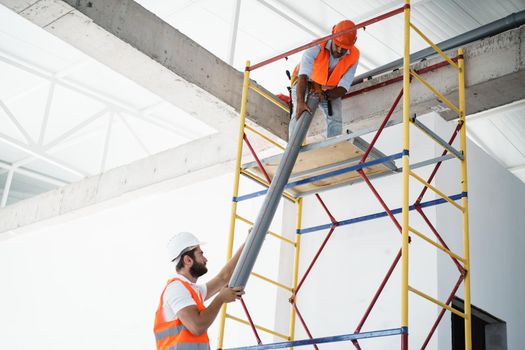 Two men builder in work uniform drag the pipe on scaffolding at construction site