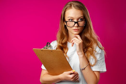 Young beautiful smiling woman standing and holding clipboard against pink background