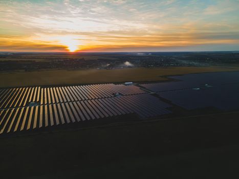 Aerial drone view into large solar panels at a solar farm in large field on countryside at bright sunset. Solar cell power plants, colorful photo