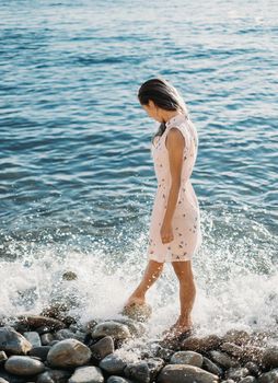Beautiful young woman walking on pebble beach near the sea, looking at sea waves