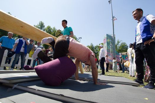 KAZAN, RUSSIA - JUNE 23, 2018: Traditional Tatar festival Sabantuy - Two men on the balance beam fighting with pillows, telephoto shot