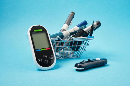 glucose meter and several different syringe pens for injections of insulin on a blue background, lancet piercing the skin to measure the level of sugar in the blood