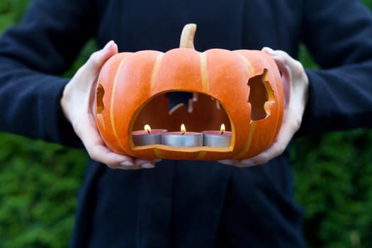 pumpkin with candle on woman hands close up-holidays, halloween, decoration and people concept