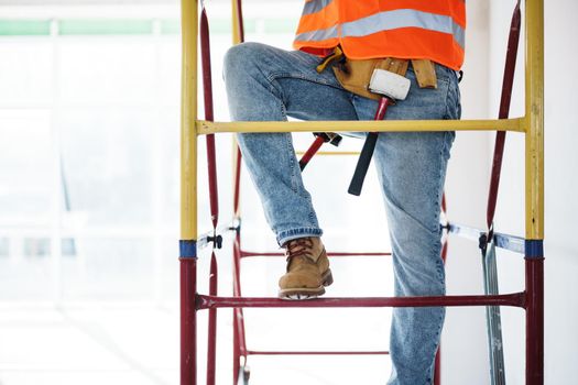 Young handsome builder climbing on scaffolding at construction site, close up