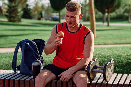 man in the park sits on a bench and eats an apple summer. High quality photo