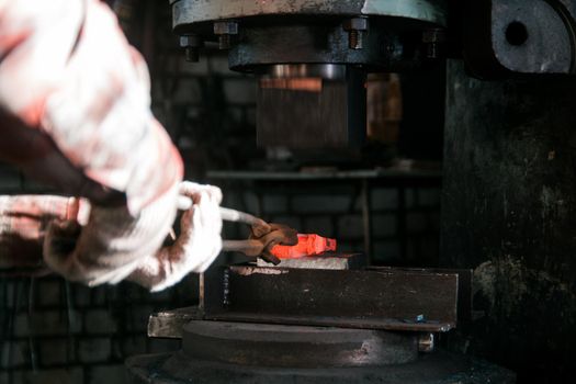 Blacksmith working with red hot metal workpiece of new axe on the anvil and electro hammer at the forge. Focus on anvil. Close up shot