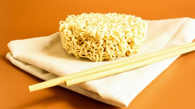 raw instant noodles on a towel with chopsticks on a yellow background. pasta, for the preparation of which it is enough to pour boiling water over it and wait a few minutes. Copy space